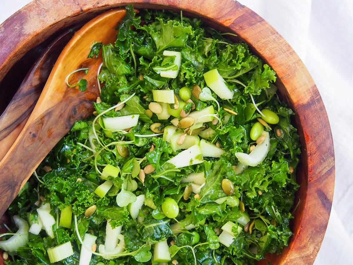 wooden bowl with apple kale salad and salad servers to side of bowl