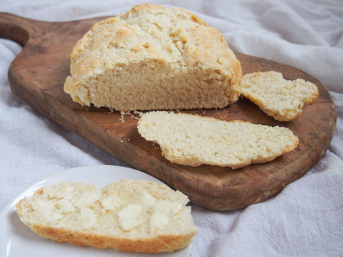slice of Australian damper bread with butter on plate in front of loaf and slices on board