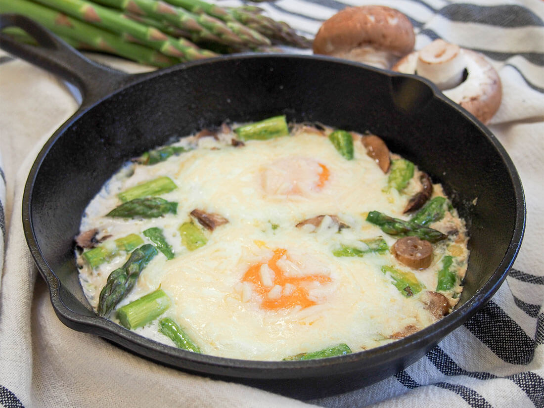 Baked eggs with mushrooms and asparagus in skillet with asparagus and mushroom behind