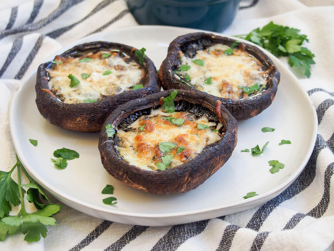 plate of three baked portobello mushrooms topped with cheese and a little parsley on top