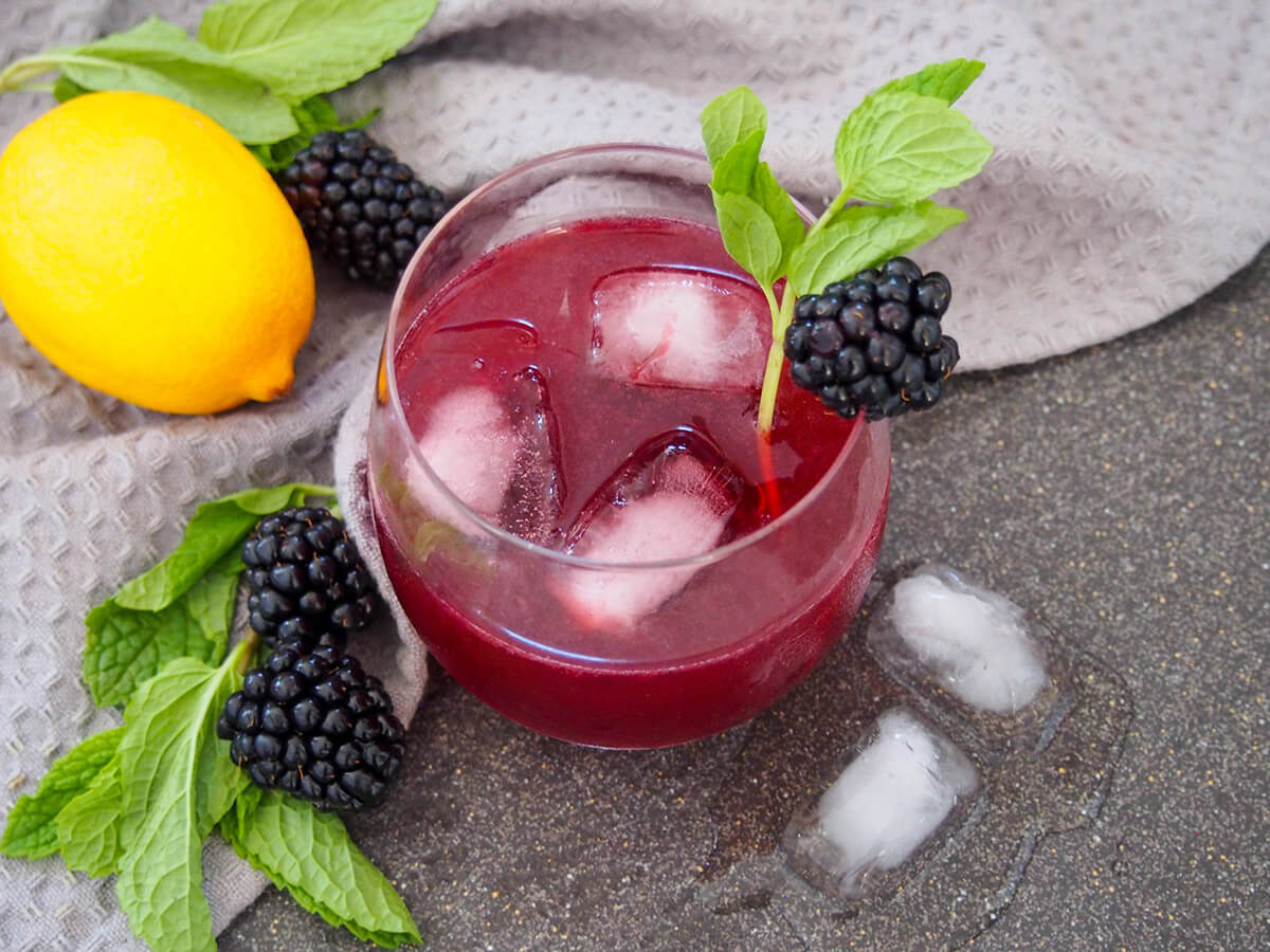 glass of blackberry bourbon smash with lemon, blackberries and mint to side