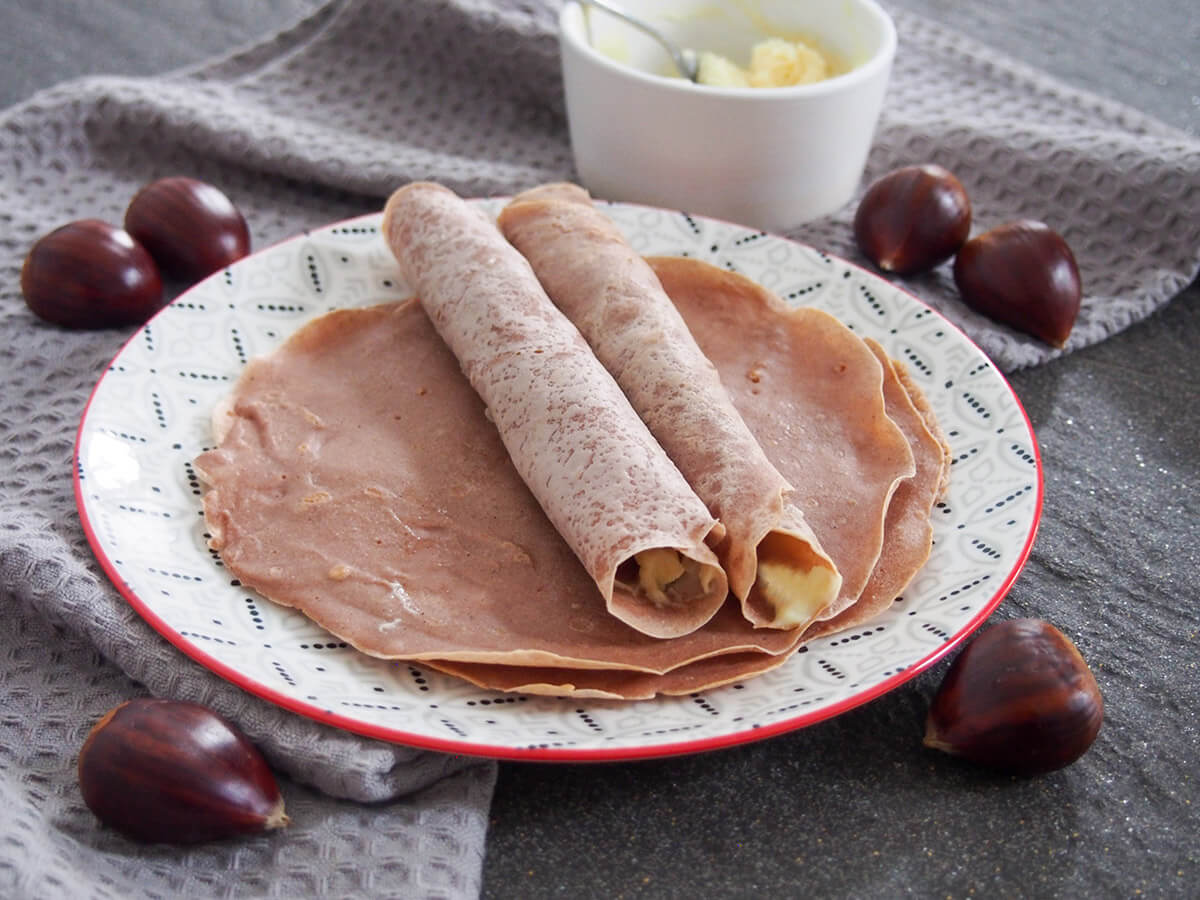two rolled up chestnut crepes on top of more on plate with chestnuts around plate