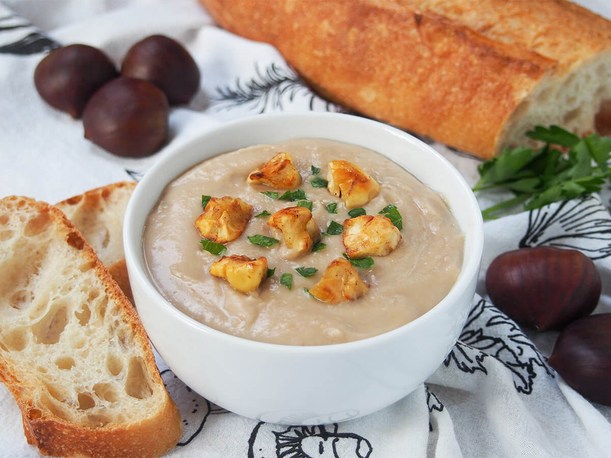 bowl of chestnut soup with slices of bread to side and chestnuts behind.