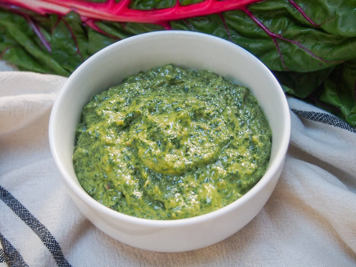 bowl of creamy chard pesto with part view of chard leaf behind