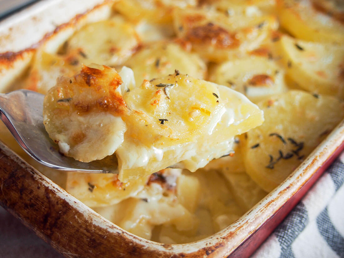 spoonful of Dauphinoise potatoes held in front of dish filled with rest