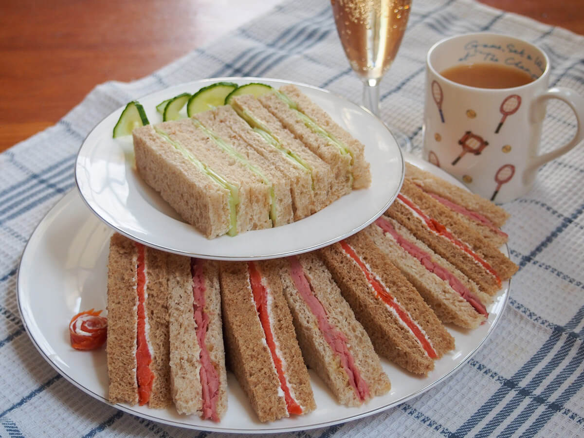 stacked plates with English tea sandwiches with cup of tea behind