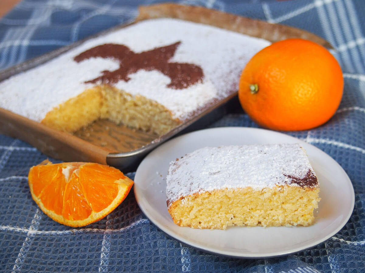 slice of Florentine orange cake schiacciata on plate in front of rest and orange behind plate