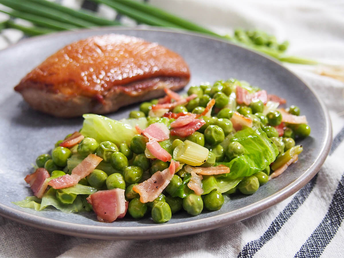 Petits pois a la francaise French peas on plate with seared duck breast behind