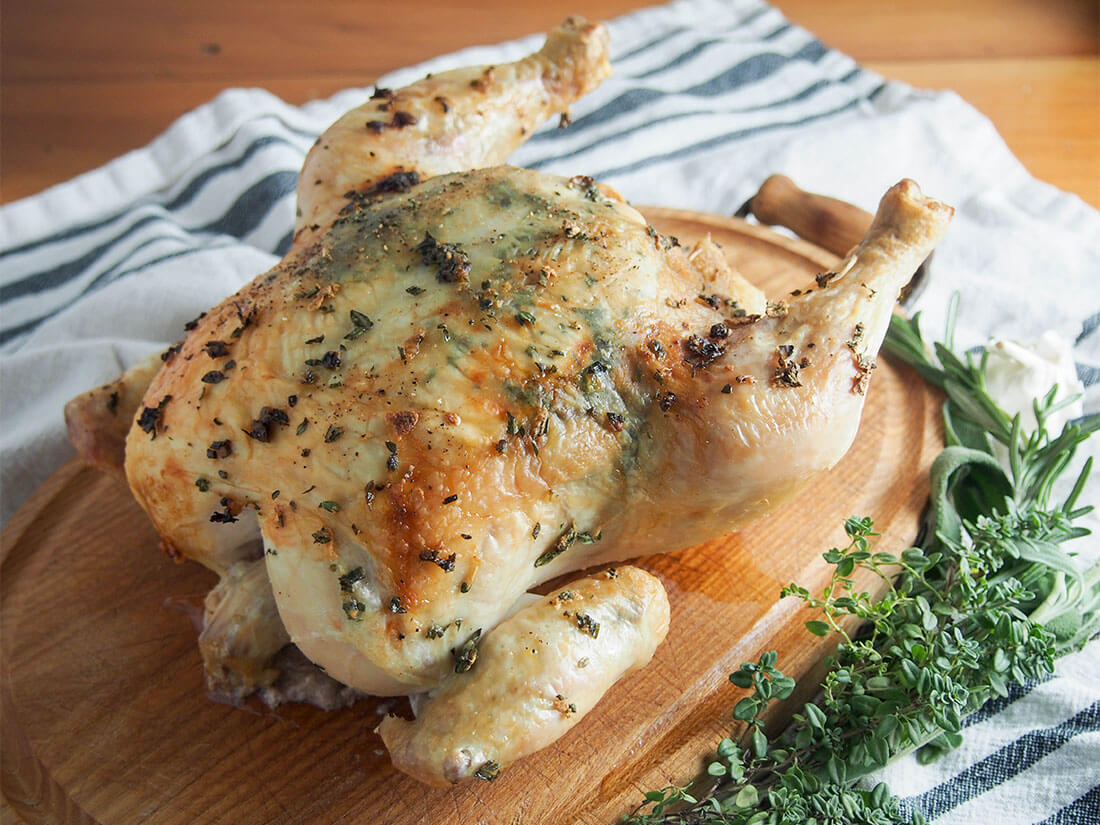 garlic herb roasted chicken on board with fresh herbs to side