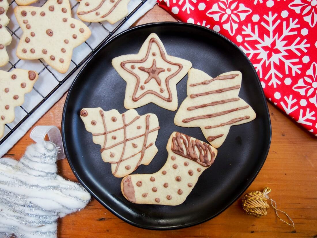 black plate with four German ginger cookies with others on rack to side, and some Christmas decorations on other sides