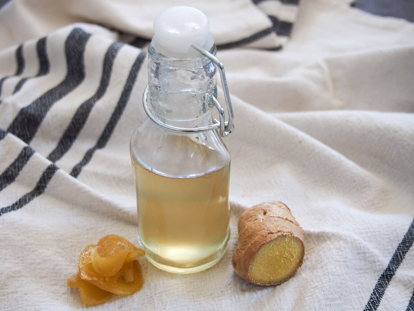 bottle of ginger syrup with piece of fresh ginger to side