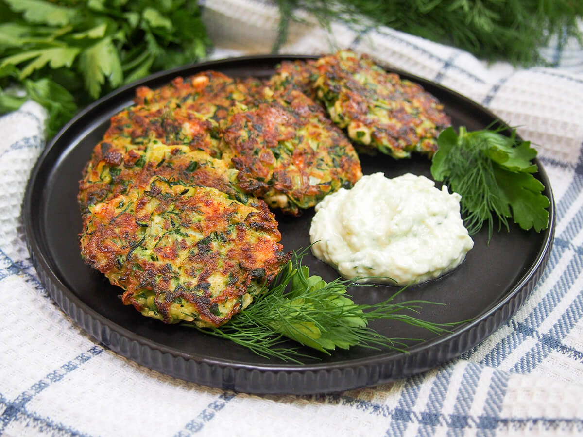 plate of Greek zucchini fritters (kolokithokeftedes) with herbs at front and yogurt sauce to side
