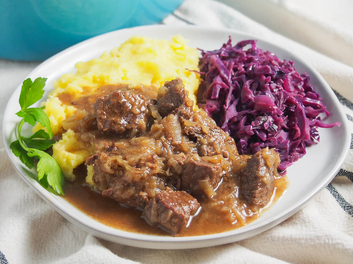 plate of hachee Dutch beef stew served with red cabbage and mashed potato behind.