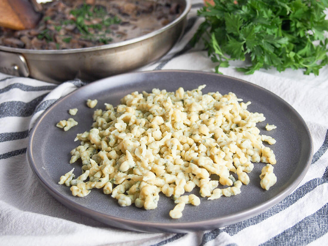herb spaetzle on plate with herbs and dish with mushroom stroganoff behind