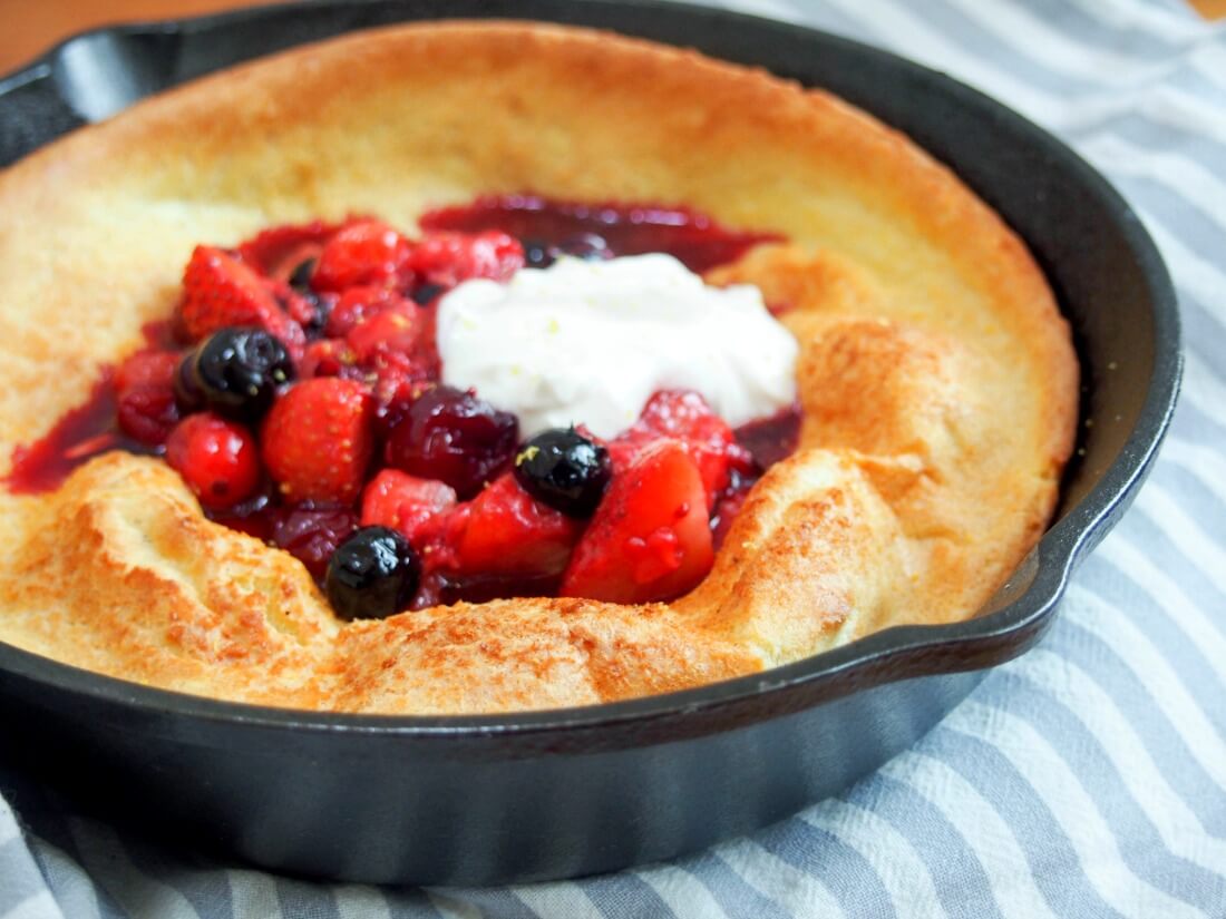 individual Dutch baby pancake in skillet topped with berries and maple yogurt