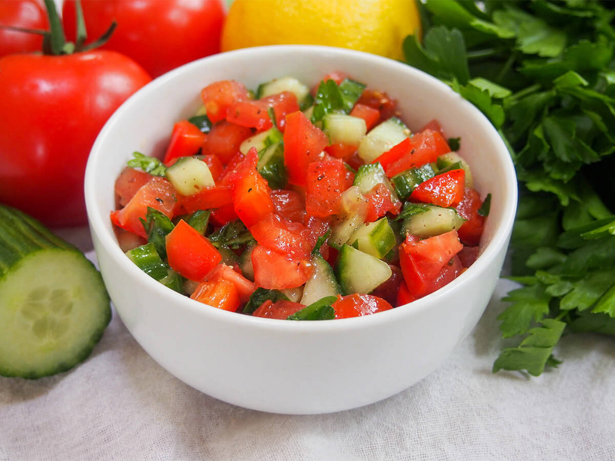 bowl of Israeli salad with cucumber and tomato one side and parsley bunch to right