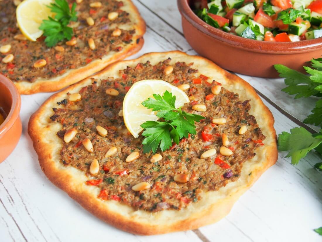 Lahmacun - Turkish flatbread - with part view of a second one behind and dish with salad