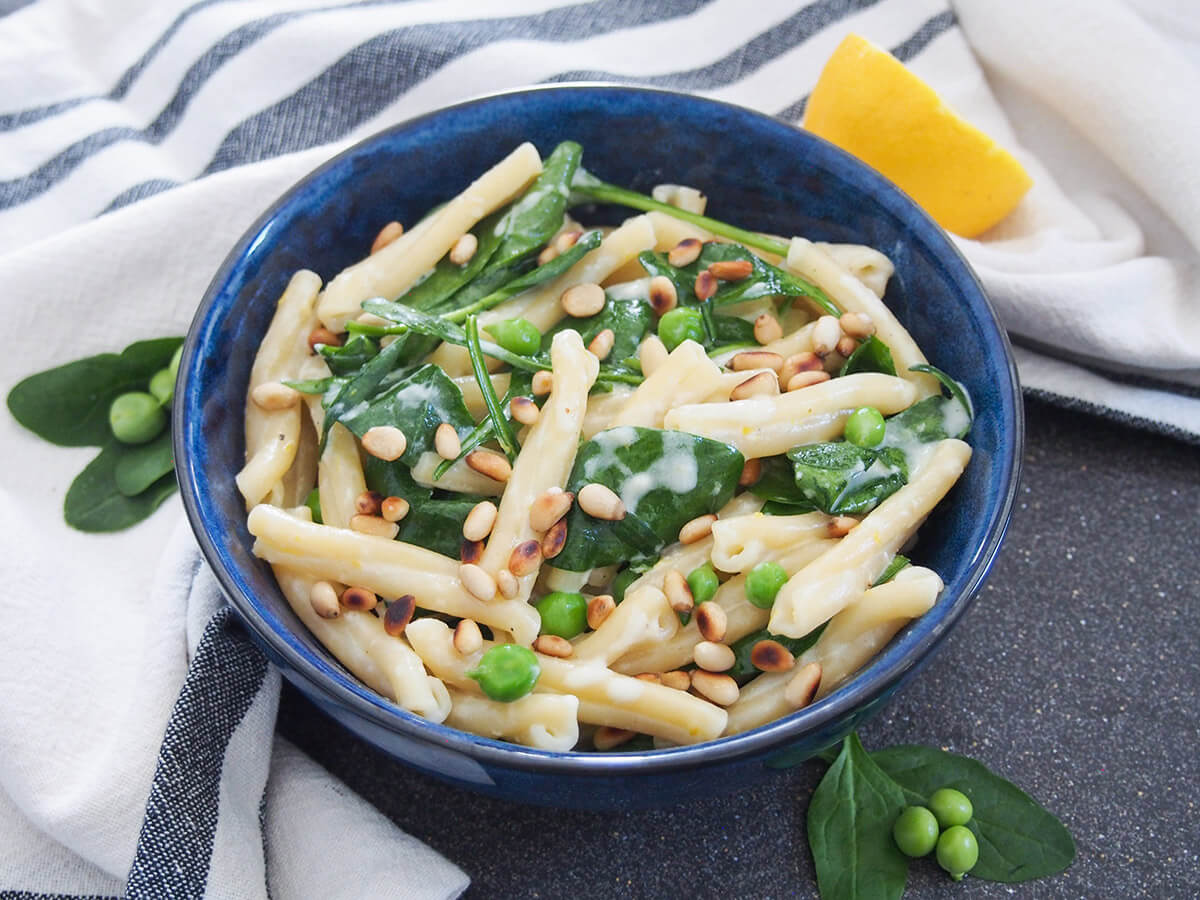 bowl of lemon mascarpone pasta with some peas and spinach leaves to side of bowl