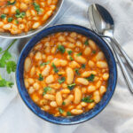 bowl of loubia Moroccan white bean stew from overhead with spoons above.