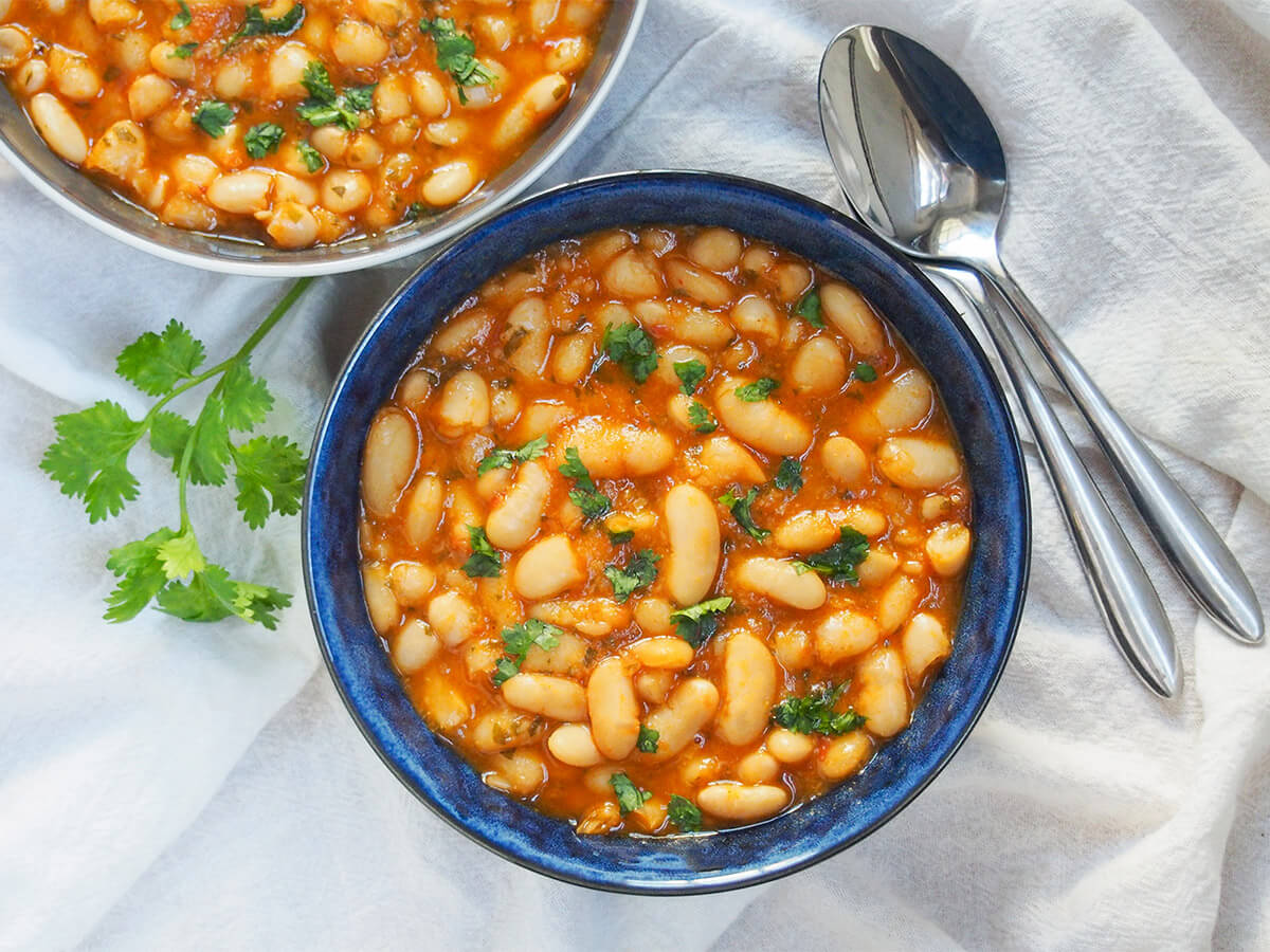 bowl of loubia Moroccan white bean stew from overhead with two spoons to right side