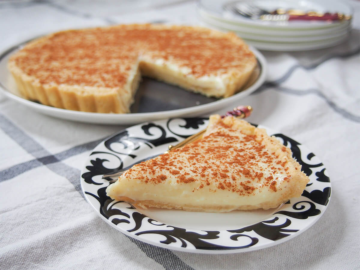 slice of South African milk tart (melktert) in front with rest of tart on plate behind.