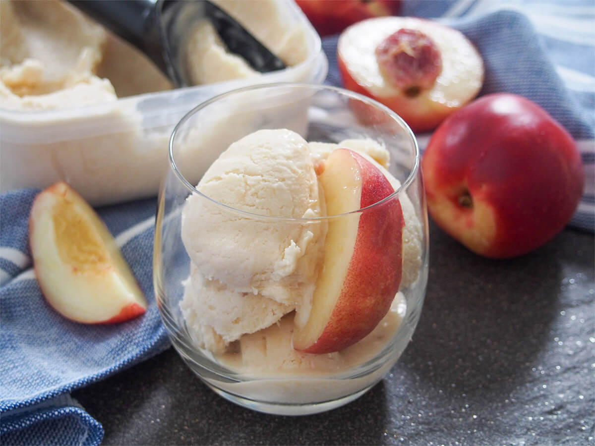 glass of nectarine ice cream with whole nectarine and slices to side and tub behind