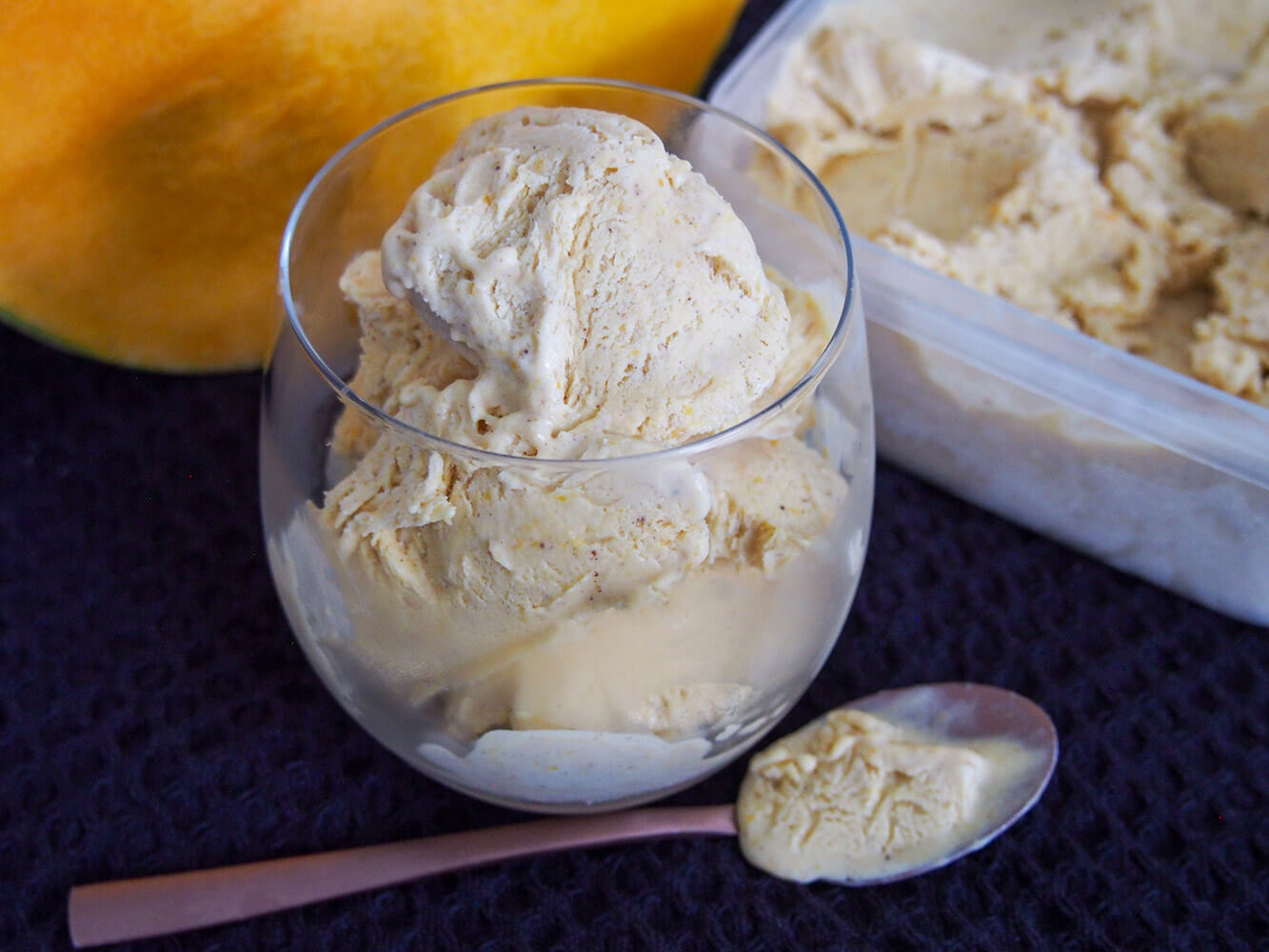 glass of no churn pumpkin ice cream with spoon under and tub behind