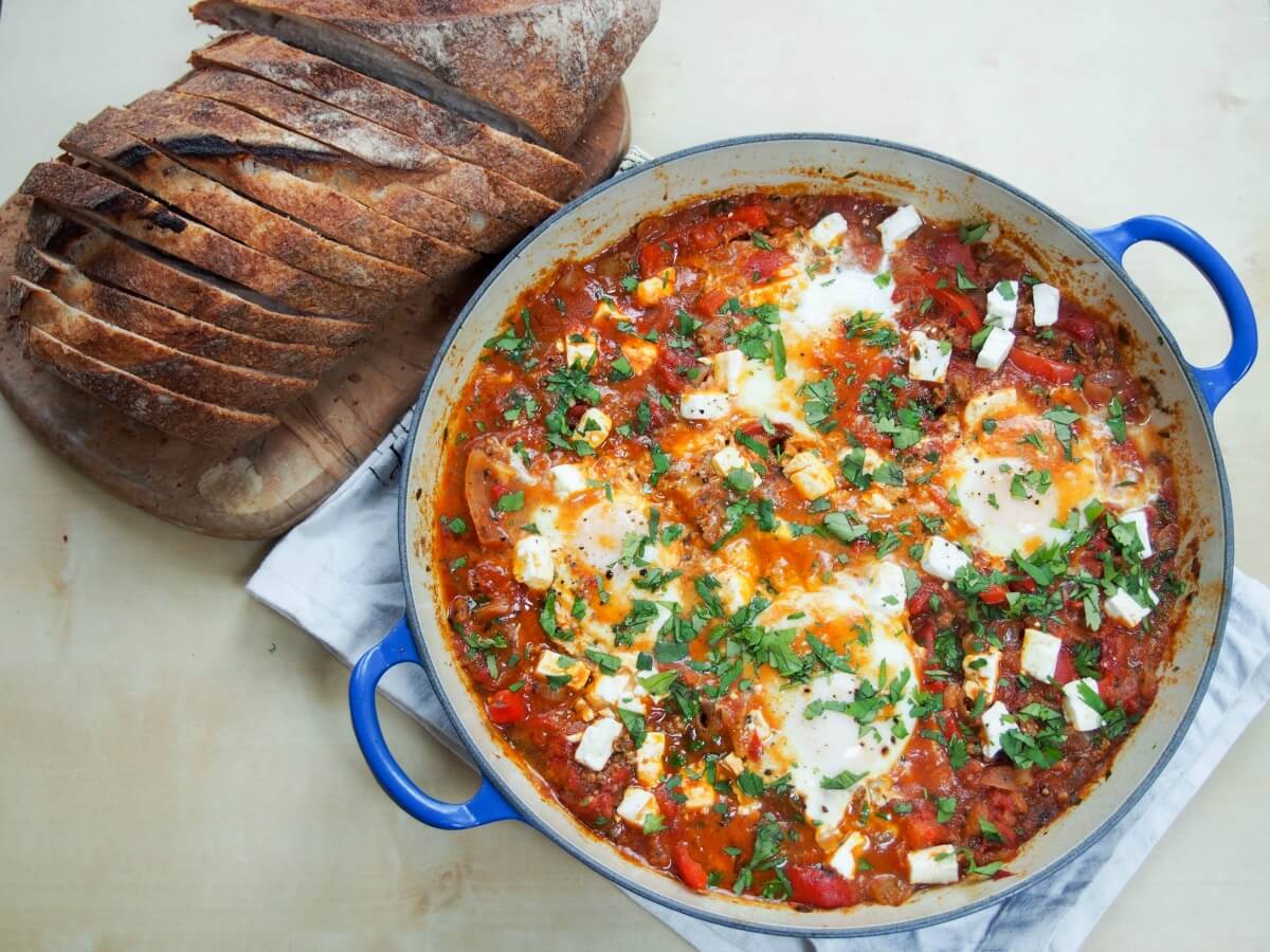 shakshuka with meat in dish with sliced loaf of bread to side
