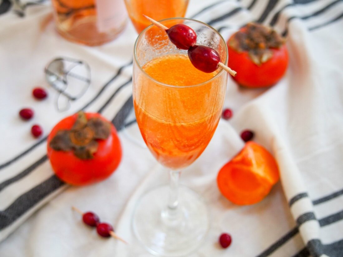 glass of persimmon apple cider mimosa with persimmon and cranberries around glass