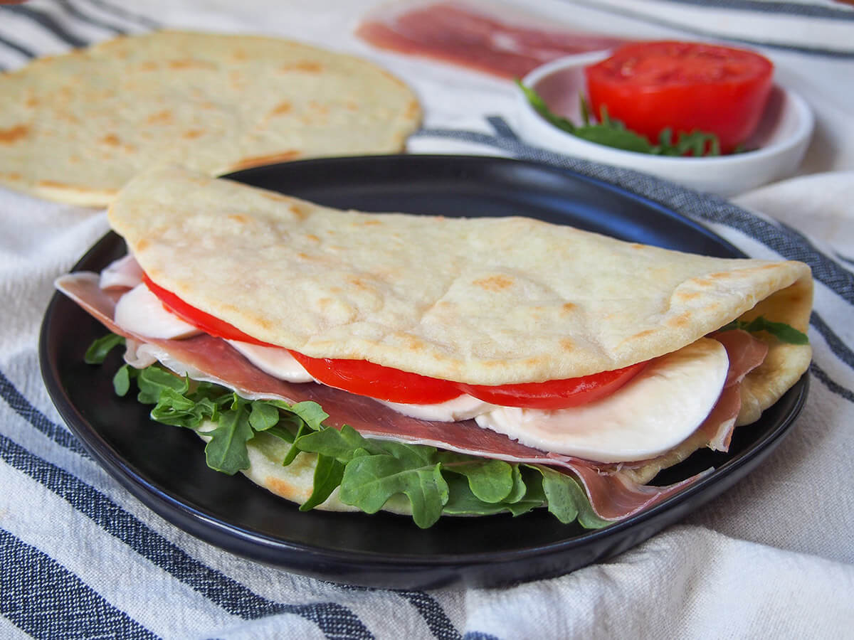 folded over piadina Italian flatbread with fillings of tomato, mozzarella, prosciutto and arugula showing