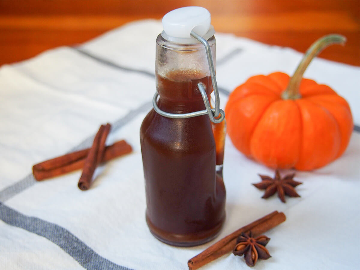 bottle of homemade pumpkin spice syrup with spices to side and mini pumpkin behind