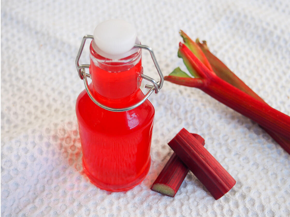 bottle of rhubarb syrup with rhubarb pieces and stems to side