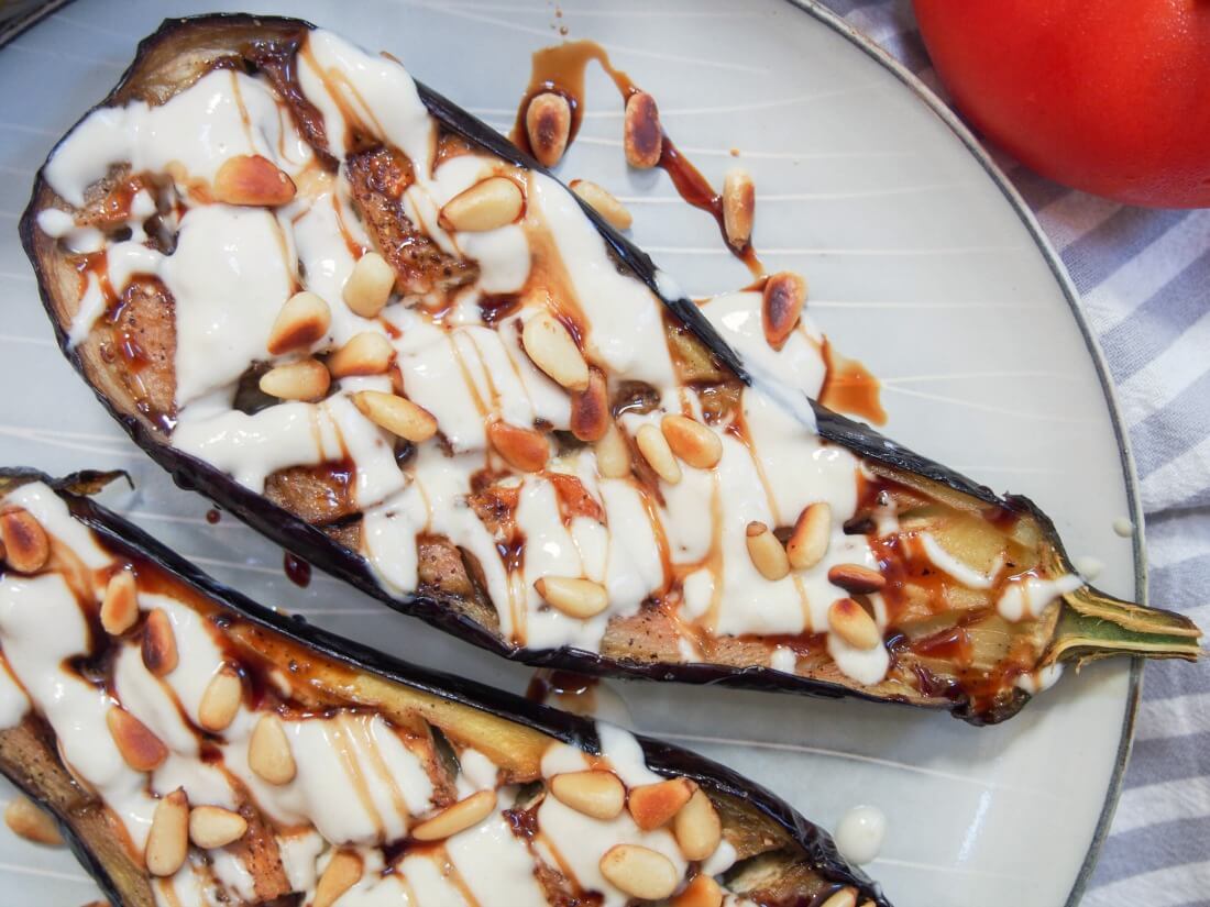 One half of a roasted eggplant with tahini drizzle, other half partially in view