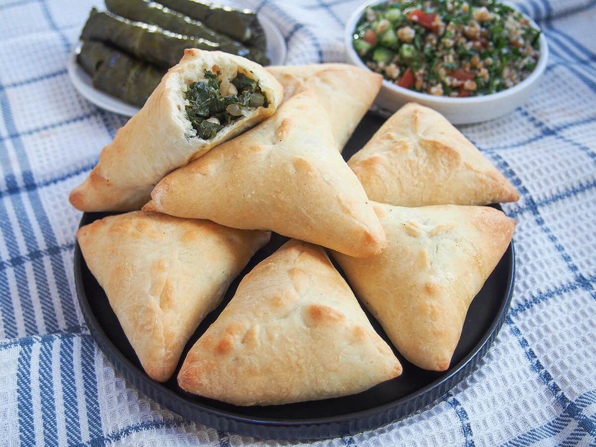 plate of spinach fatayer with plates of grape leaves and tabbouleh behind