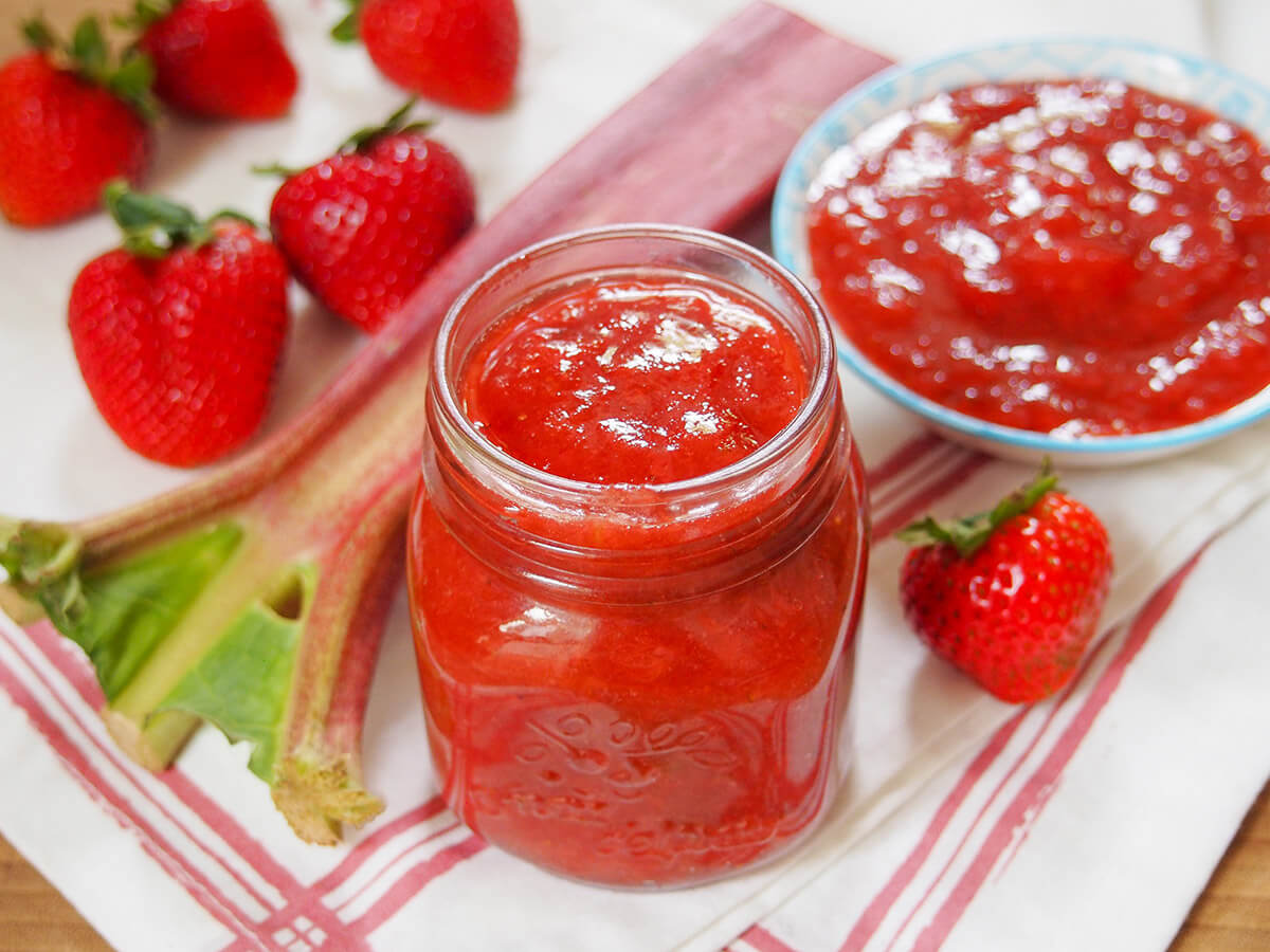jar of strawberry rhubarb jam with dosh to one side and fruit around