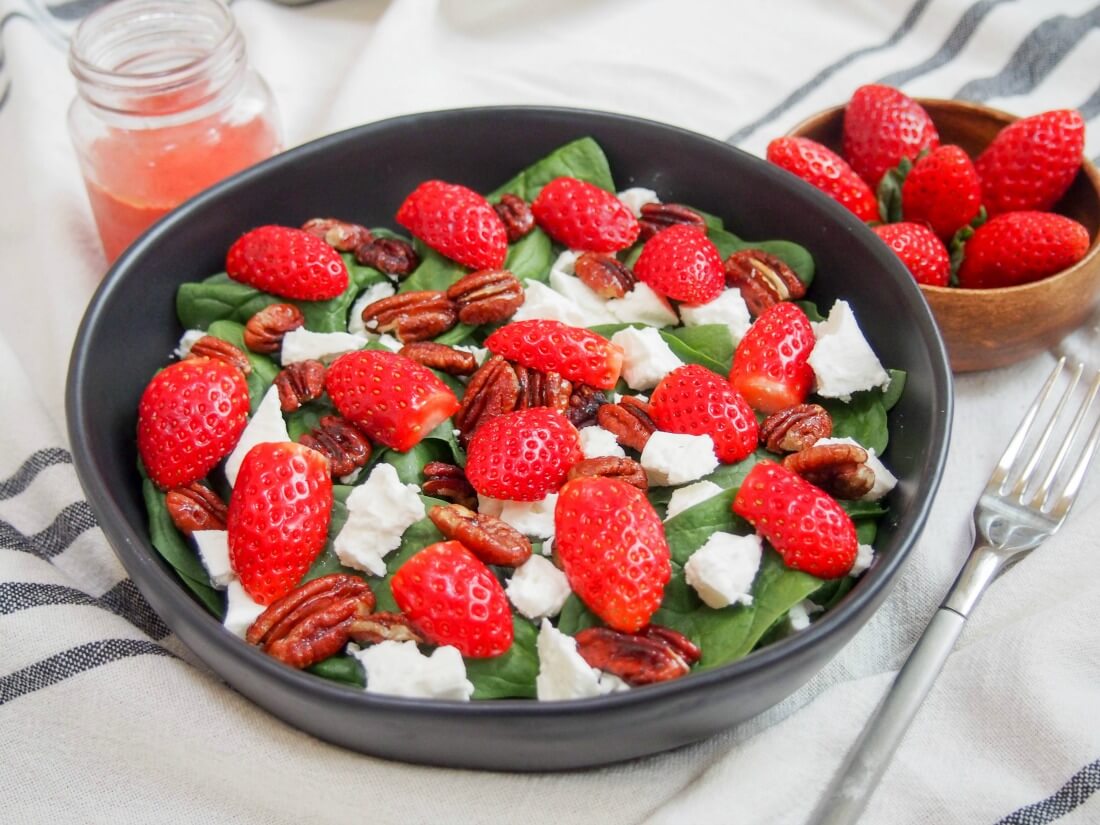 bowl of strawberry spinach feta salad with strawberries to side, dressing in jar behind and fork to side of bowl