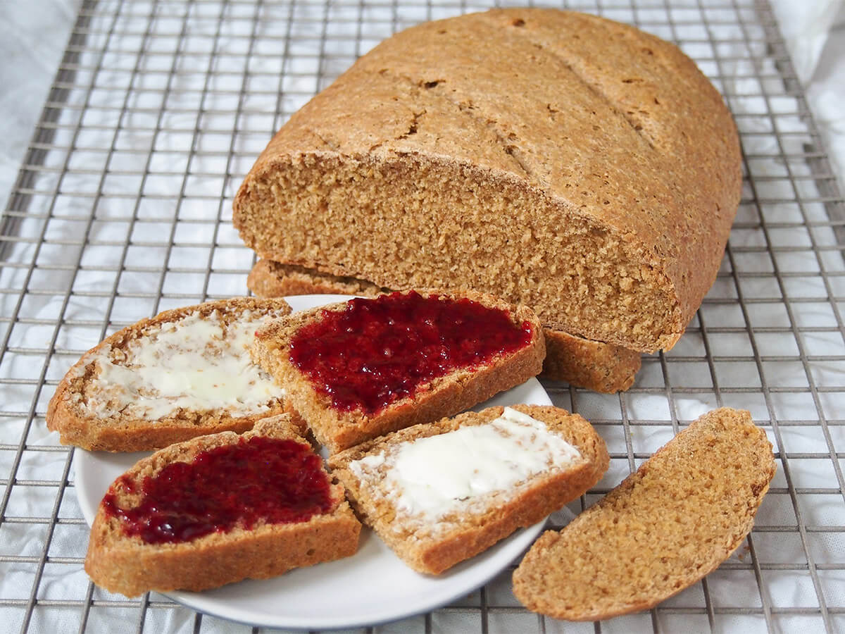 plate with slices of bread topped alternately with butter and jam and rest of Swedish limpa bread loaf behind.