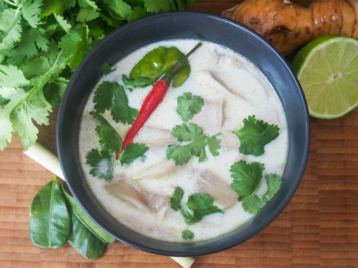 bowl of tom kha gai Thai soup from overhead with lime and other ingredients to side
