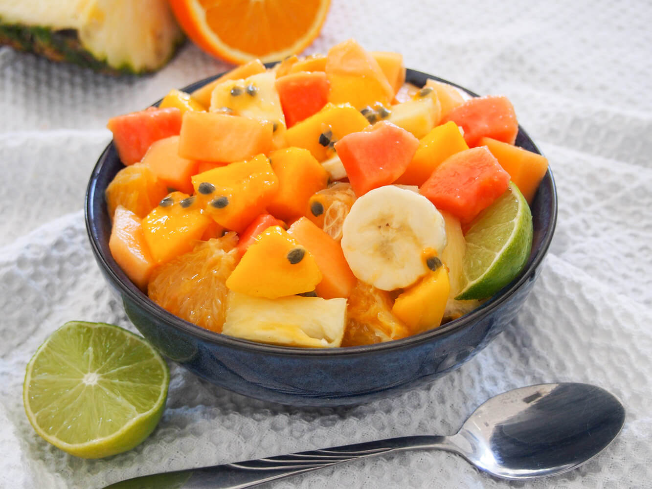 Bowl of tropical fruit salad with cut lime to side and spoon in front